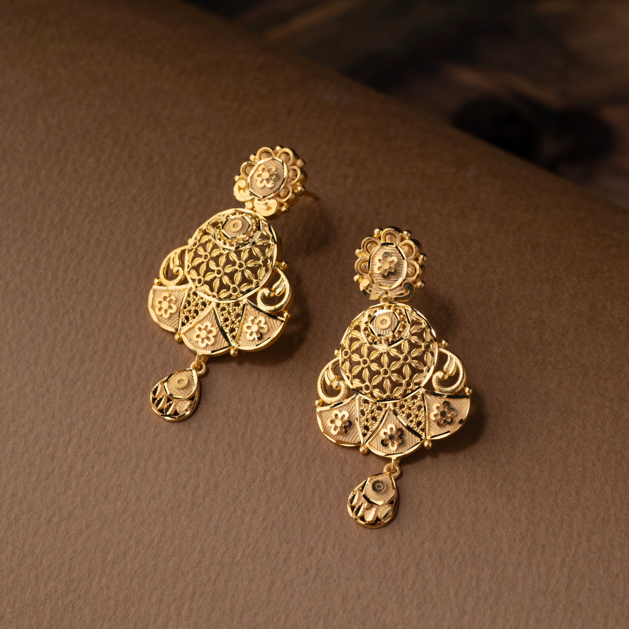 Pair of gold earrings on a brown surface. Gold replica Rani Har necklace and earrings. Gold forming jewellery, gold plated jewellery, Triyanka by Tilloma