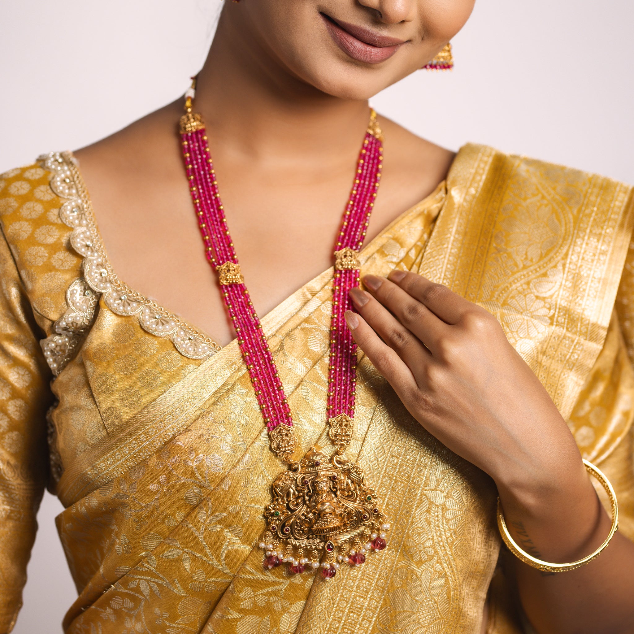 Woman wearing a gold saree with a pink beaded South Indian Temple necklace and earrings.