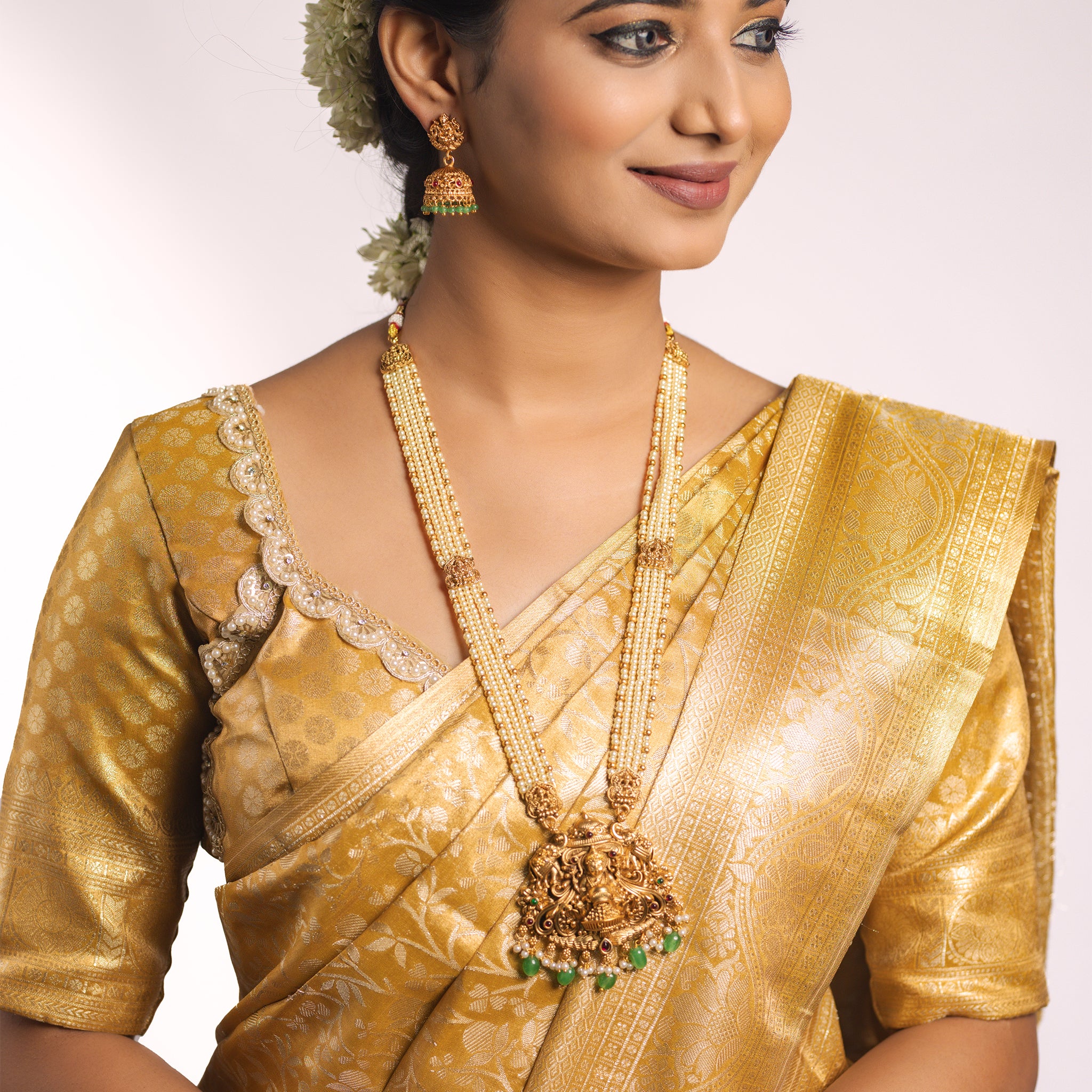 Woman wearing a gold saree with Off white temple jewelry Lakshmi on a plain background