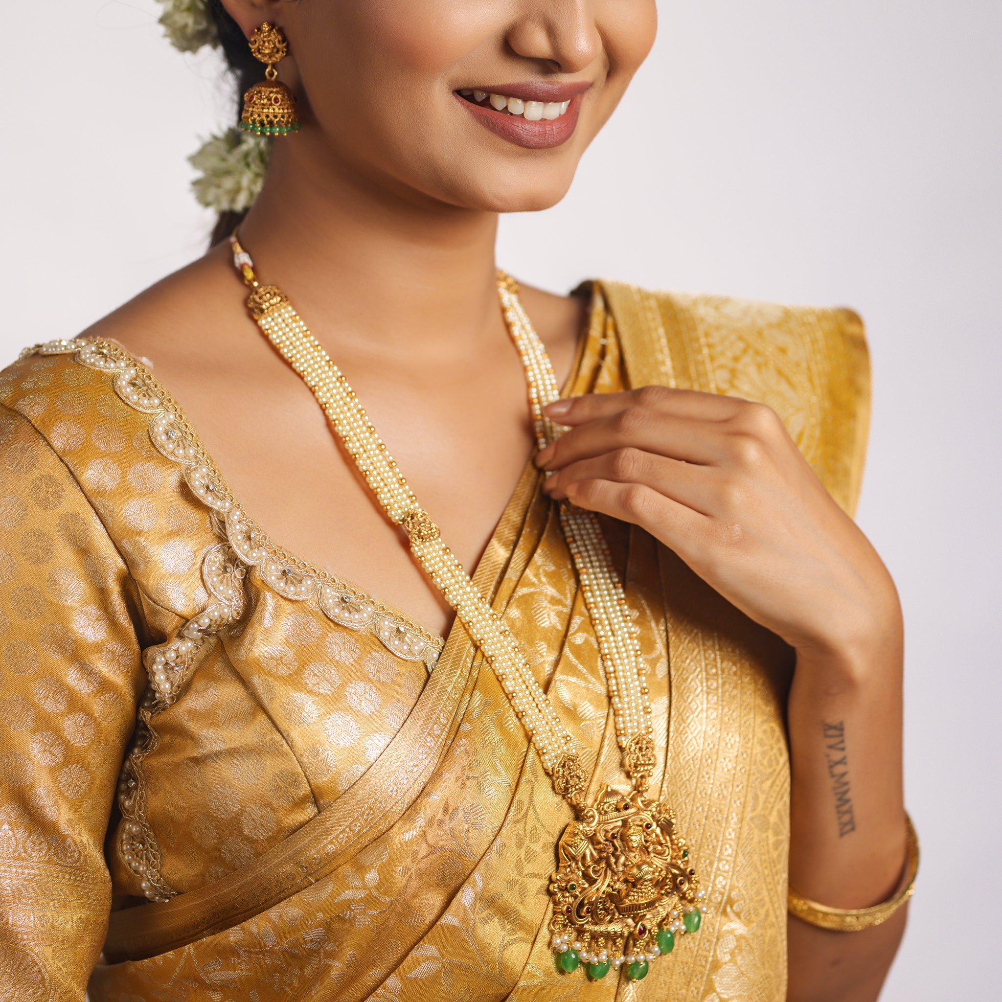 Woman wearing a gold saree with a matching South Indian Temple necklace and earrings on a white background