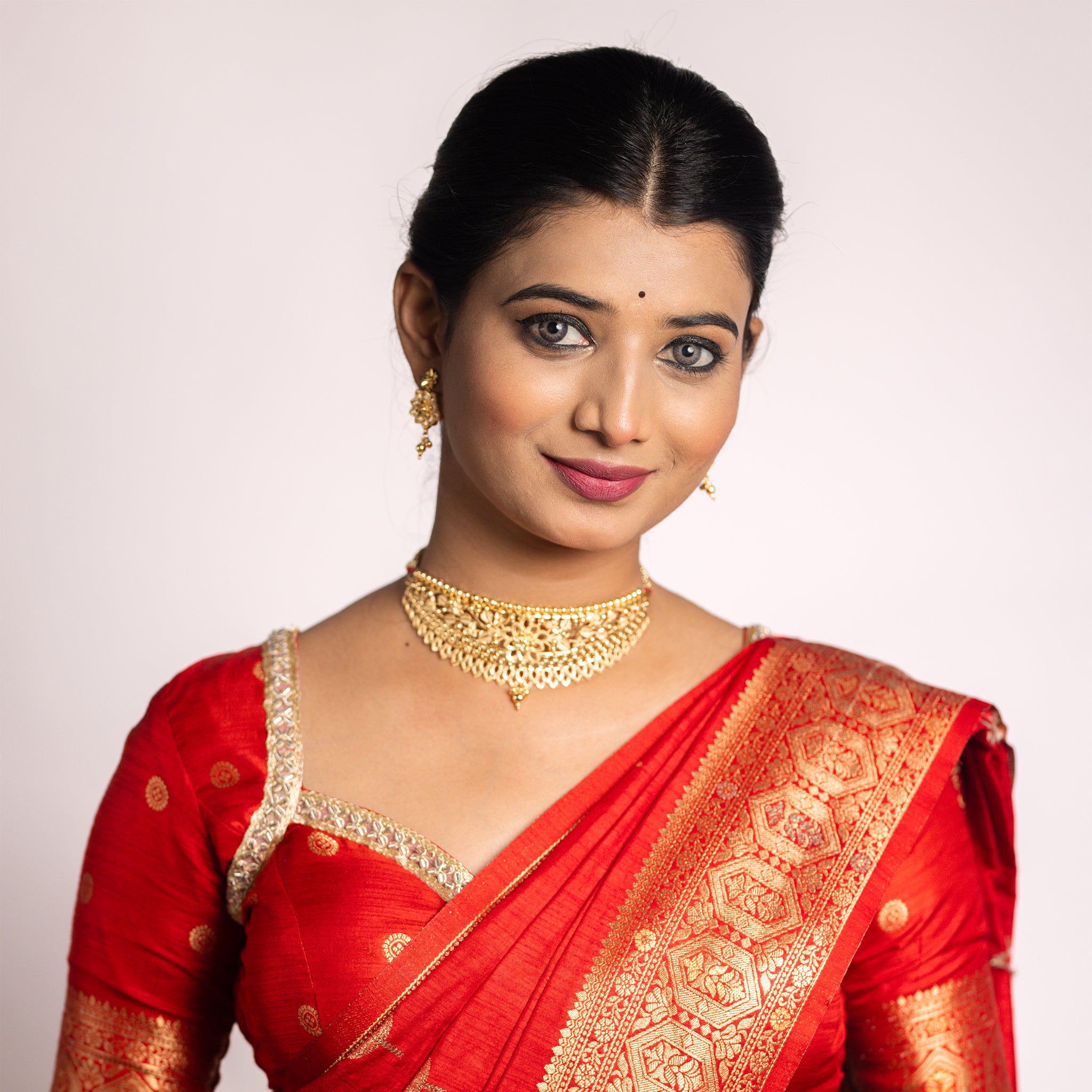 Woman wearing gold jewelry including earrings and a choker necklace, with a red garment. Gold Choker, forming jewellery, Poovi by Tilloma