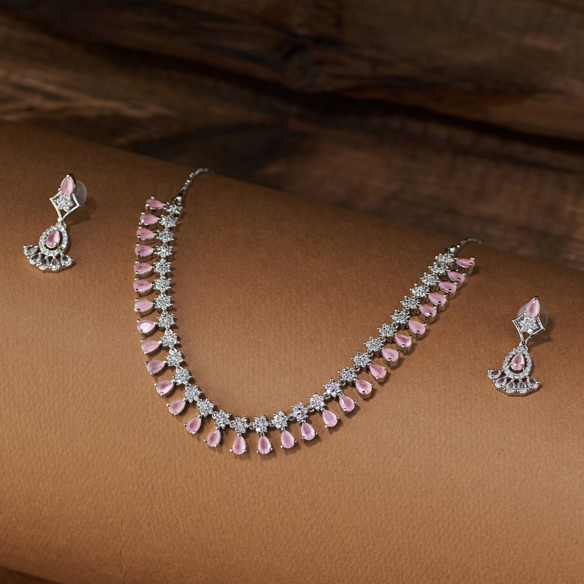 Teardrop Necklace and earrings with pink cubic zircon stones on a brown surface