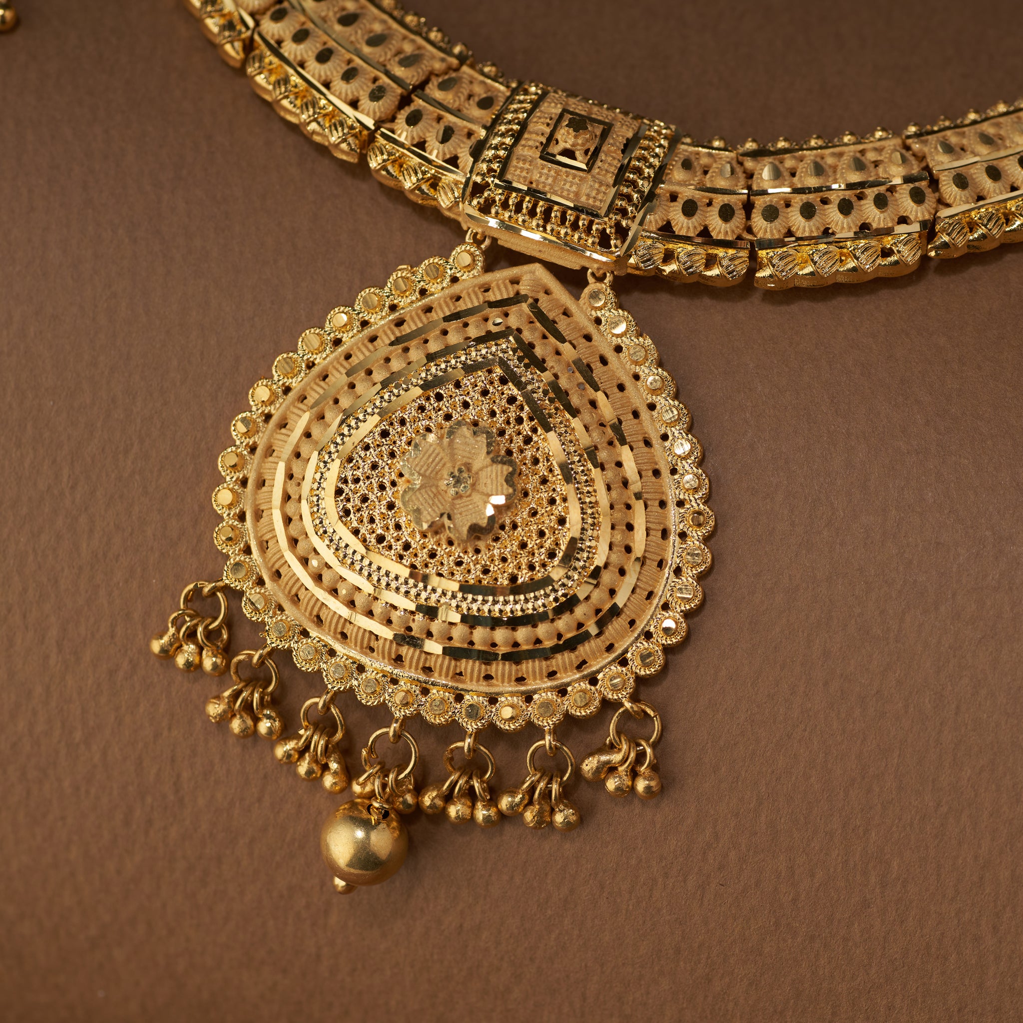 Gold necklace with intricate design on a brown background. Gold necklace and earrings set on a brown fabric background. Gold Forming jewellery, short necklace gold, Samika by Tilloma , bridal set
