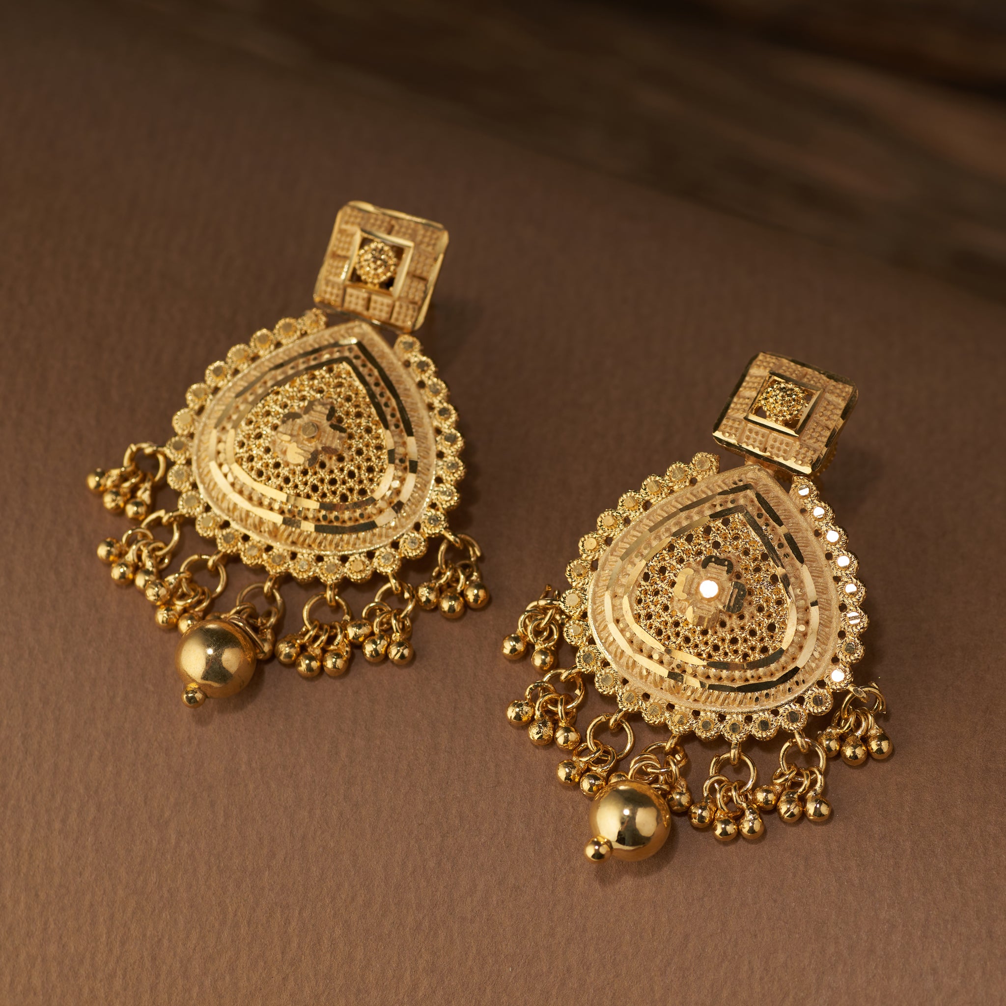 Pair of gold earrings on a brown background. Gold necklace and earrings set on a brown fabric background. Gold Forming jewellery, short necklace gold, Samika by Tilloma , bridal set