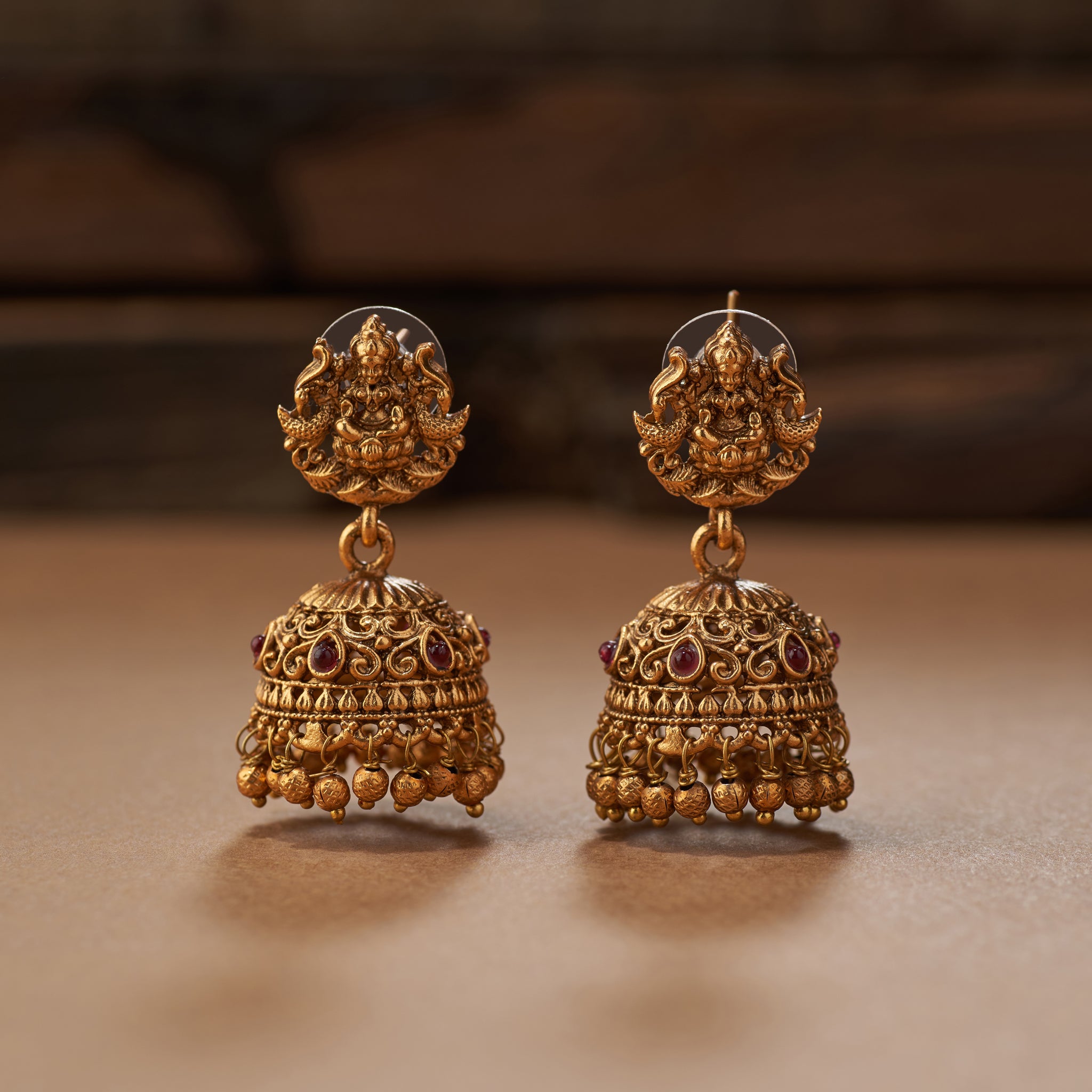 Gold necklace and earrings on a brown background. South Indian Temple jewelry with Lakshmi Motif. Temple Jewellery Lakshmi | Tilloma. Matt gold with intricate design on a brown background