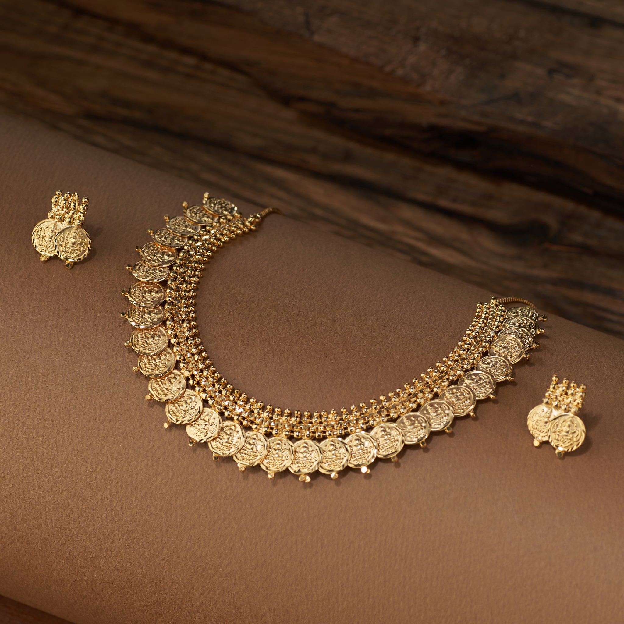 A traditional gold coin necklace set featuring a double row of detailed Lakshmi coins and a beaded chain, displayed with matching stud earrings.