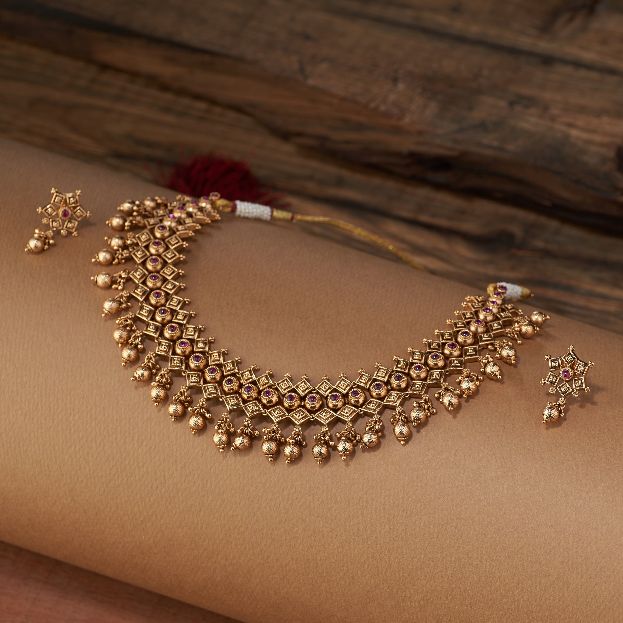 A detailed close-up of the antique gold necklace, showing the intricate geometric pattern and ruby stones of the temple jewellery design.