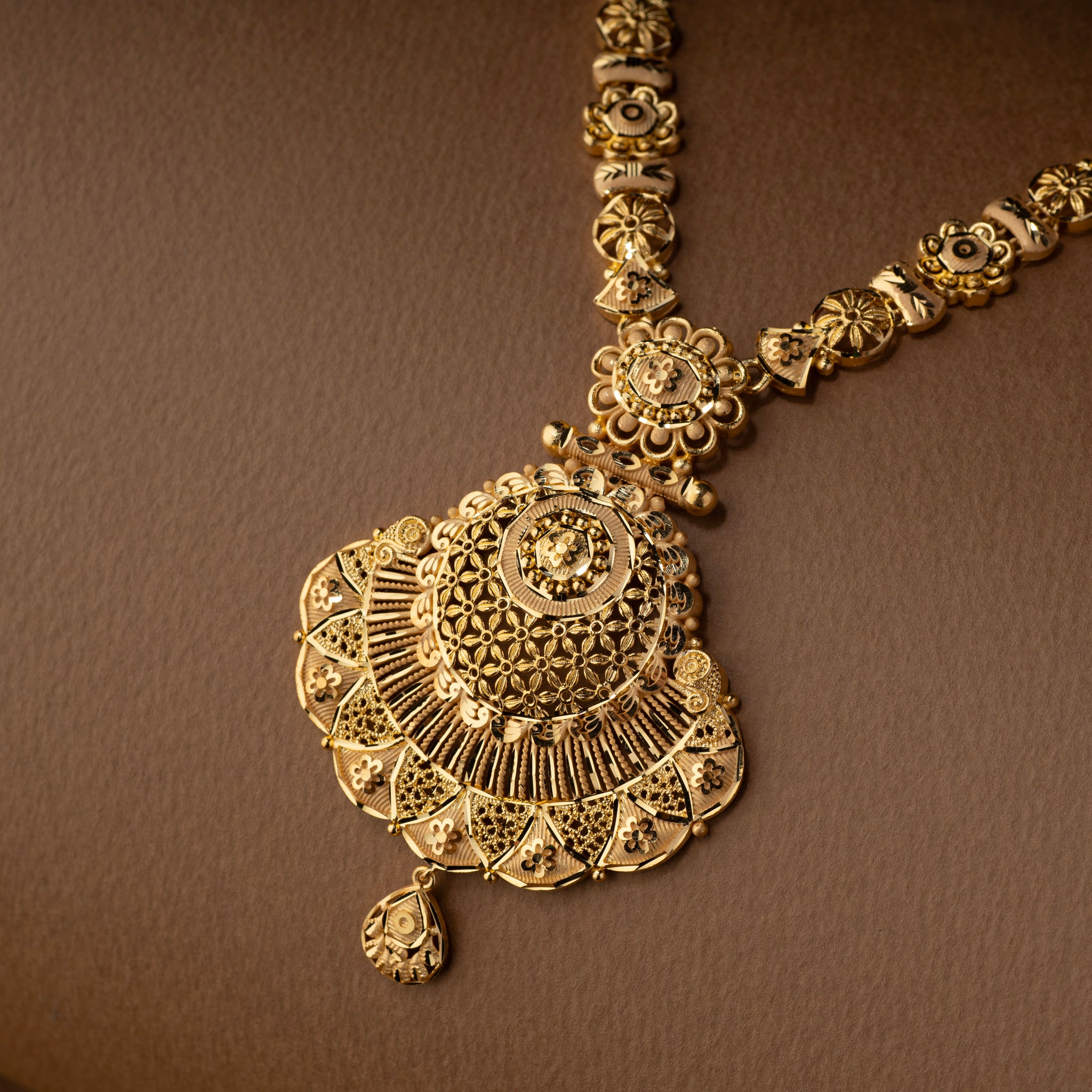 Gold necklace with intricate pendant on a brown background. Gold replica Rani Har necklace and earrings. Gold forming jewellery, gold plated jewellery, Triyanka by Tilloma.