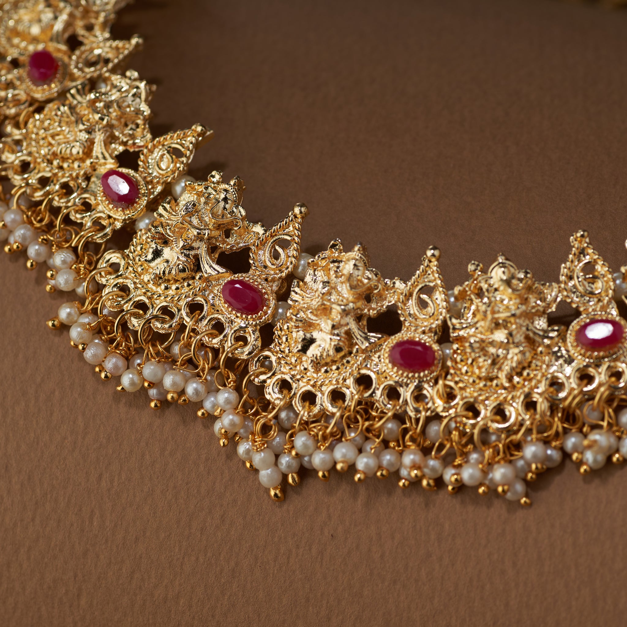 A close-up shot of the gold-plated Ganesha temple necklace, highlighting the intricate Ganesha motifs, ruby stones, and pearl drops.