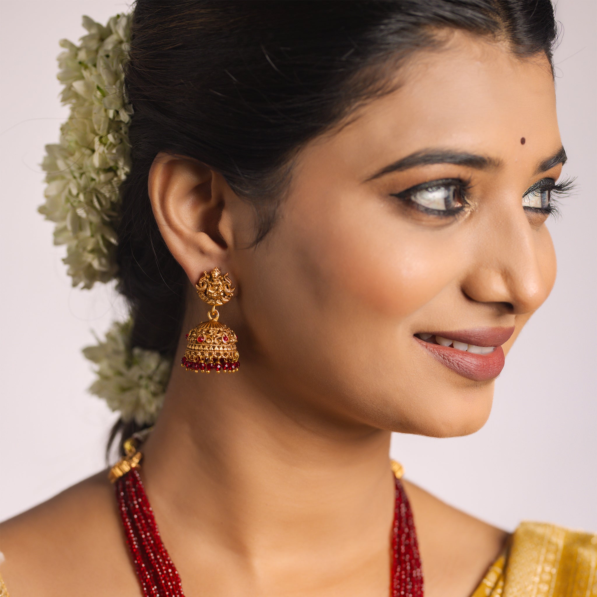 Woman wearing traditional earrings and temple jewelry with a neutral background