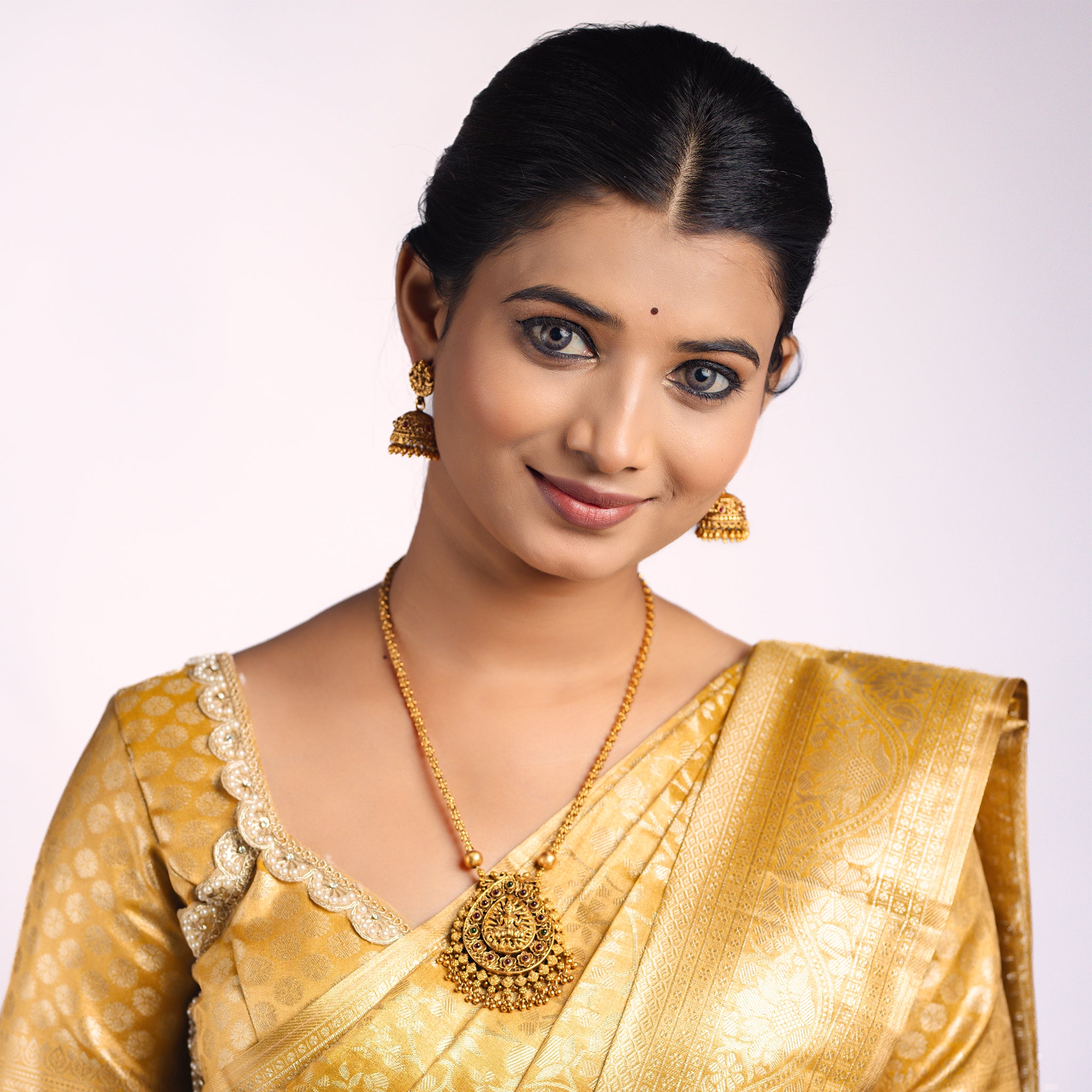 Woman wearing a gold saree with matching south Indian Temple jewelry with Lakshmi Motif. Temple Jewellery Lakshmi | Tilloma