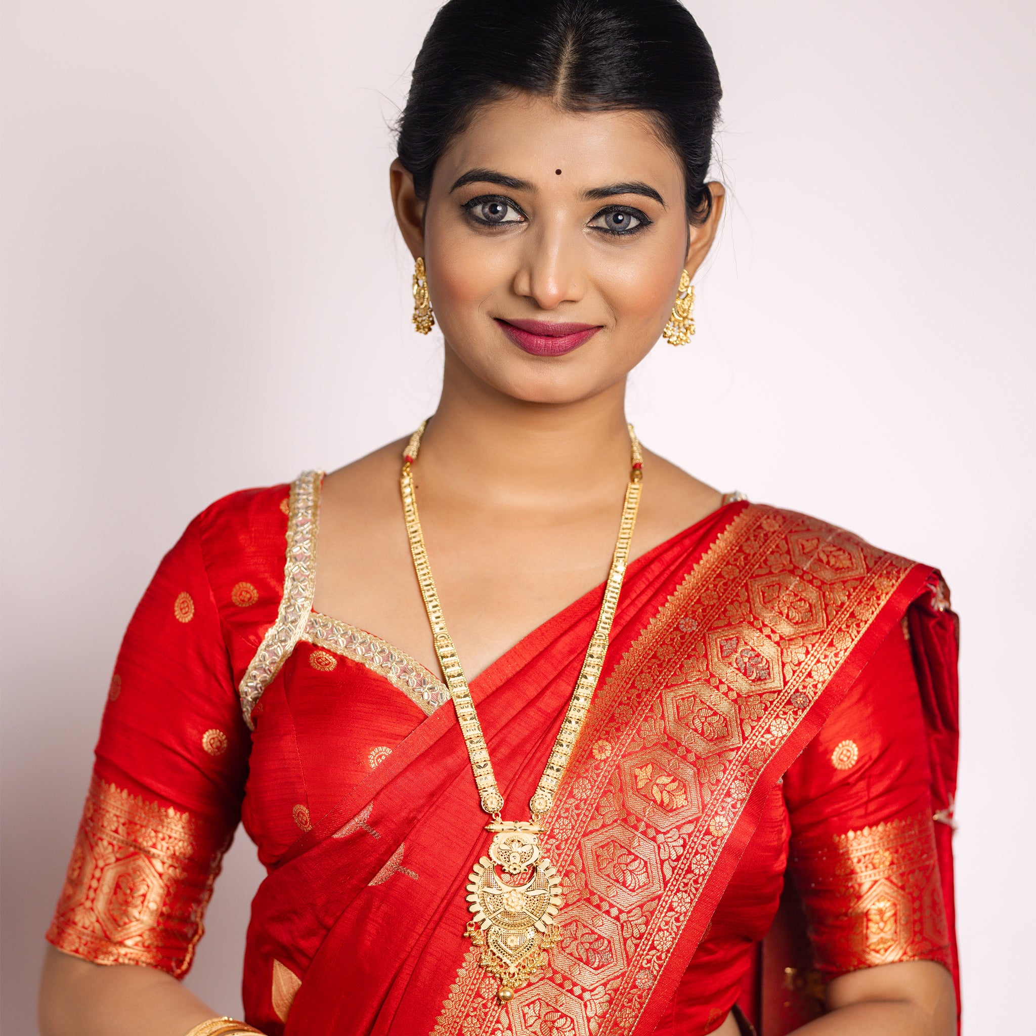 Woman wearing a red saree with gold replica necklace set. Gold Replica Rani Har Necklace Set | Rumika by Tilloma.