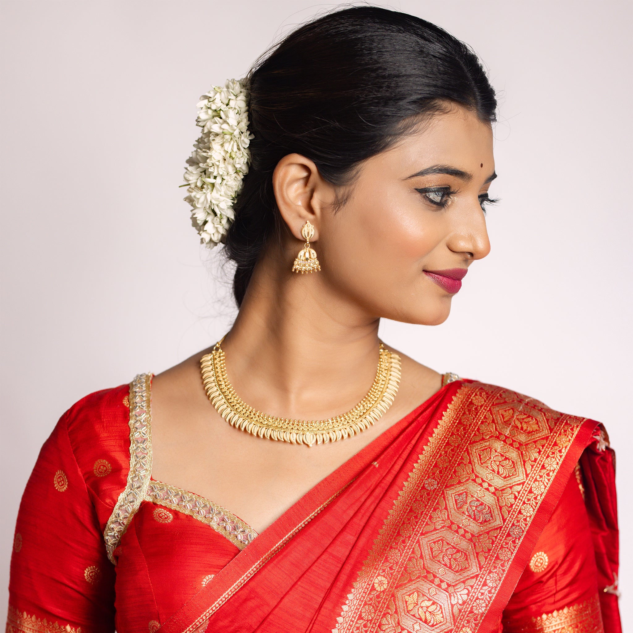Woman in a red saree with gold imitation jewelry. Gold Forming Necklace Set | Kumarika by Tilloma.