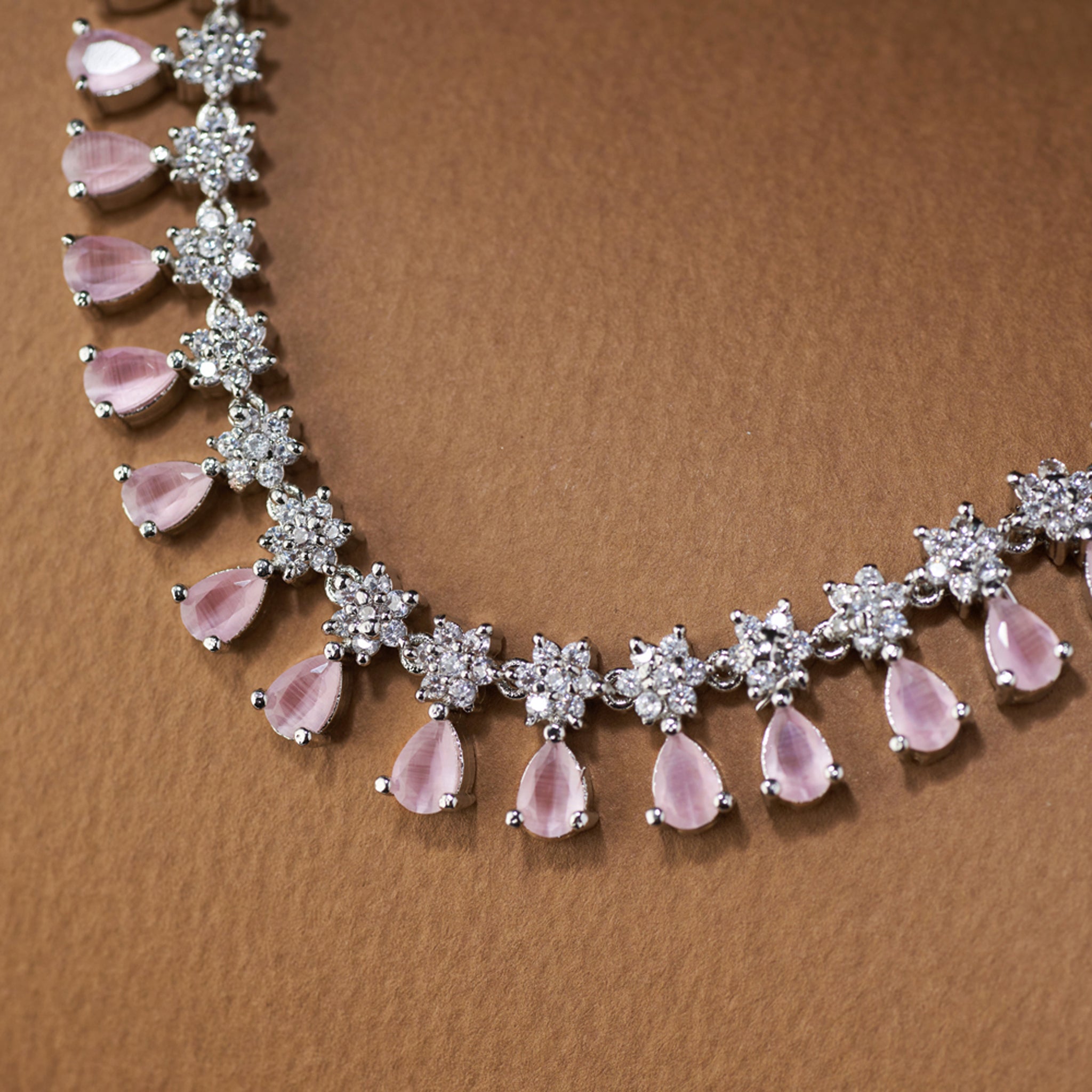 Necklace with pink teardrop-shaped stones and silver accents on a brown background