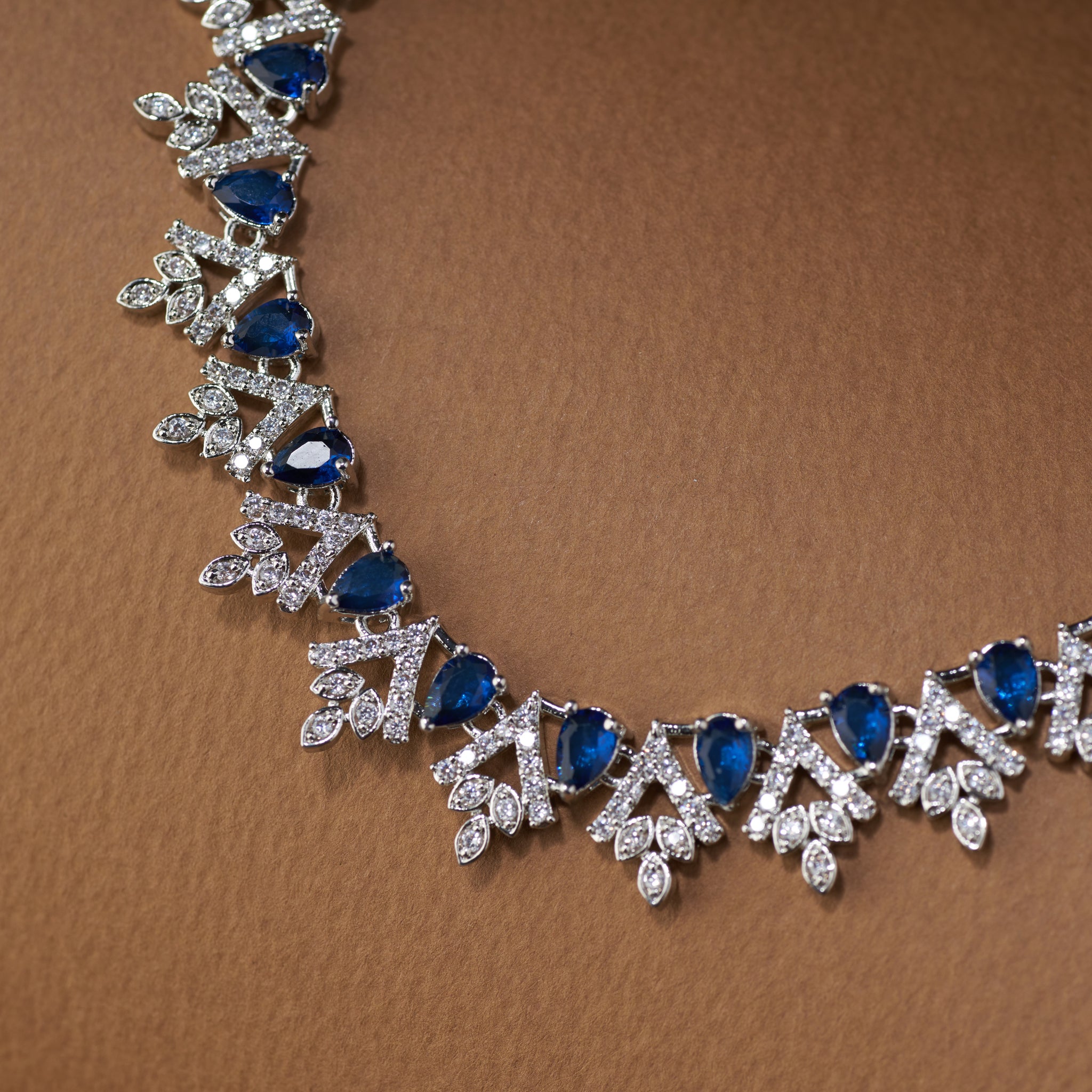 Teardrop Necklace and earrings with blue cubic zircon stones  and silver accents on a brown background