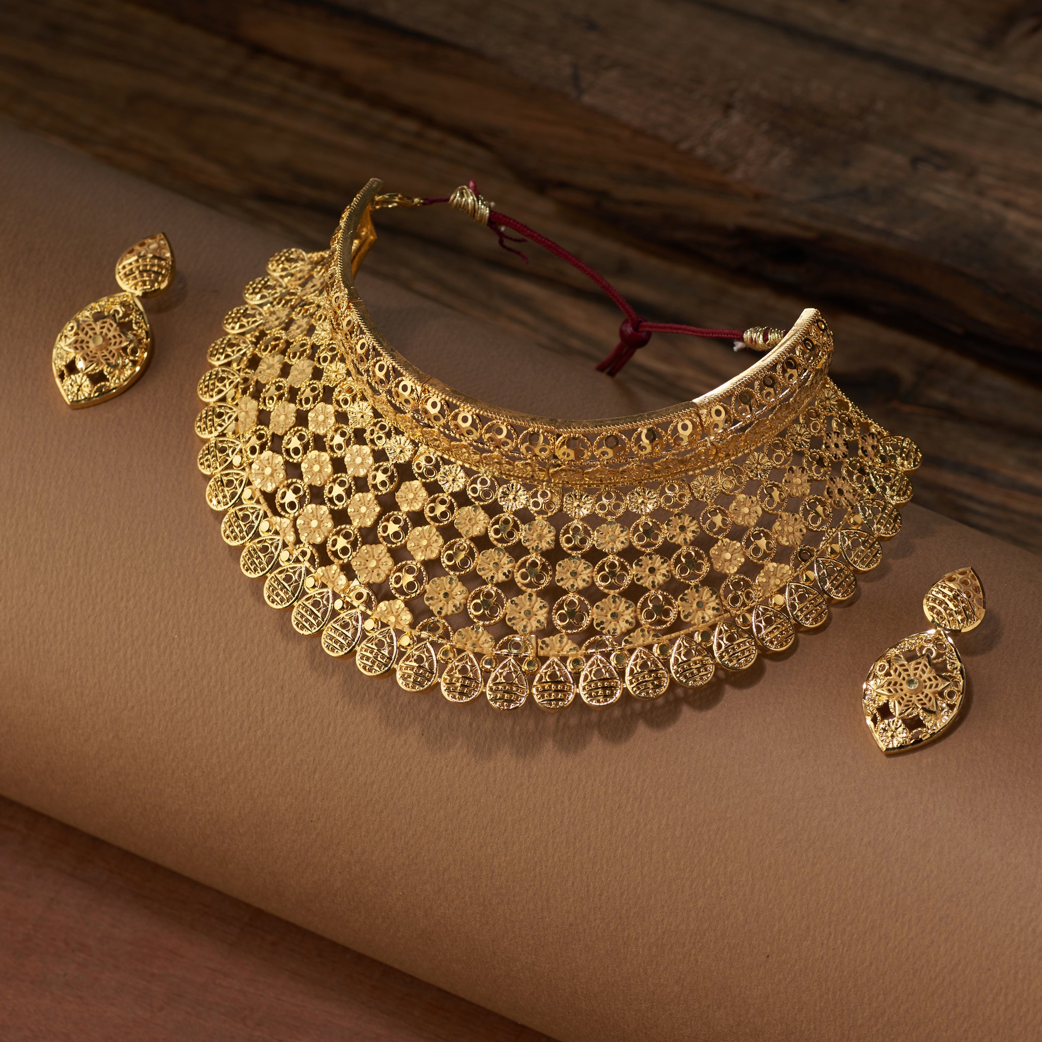 Gold choker necklace and earrings on a brown surface. Gold Choker replica, gold plated, Bridal set, Divyashri By Tilloma.