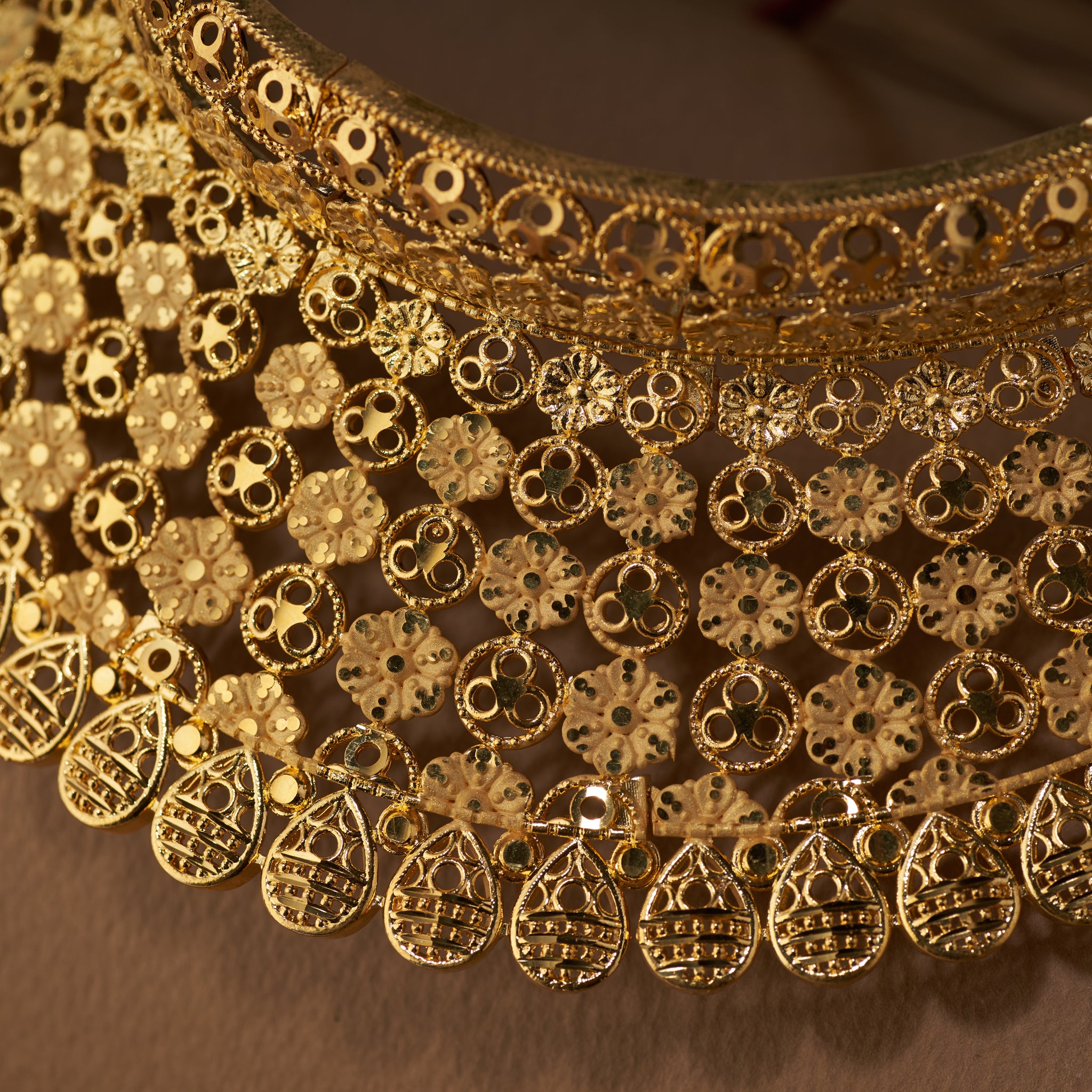 Close-up of a gold choker bridal necklace with intricate patterns. Gold choker necklace and earrings on a brown surface. Gold Choker replica, gold plated, Bridal set, Divyashri By Tilloma.