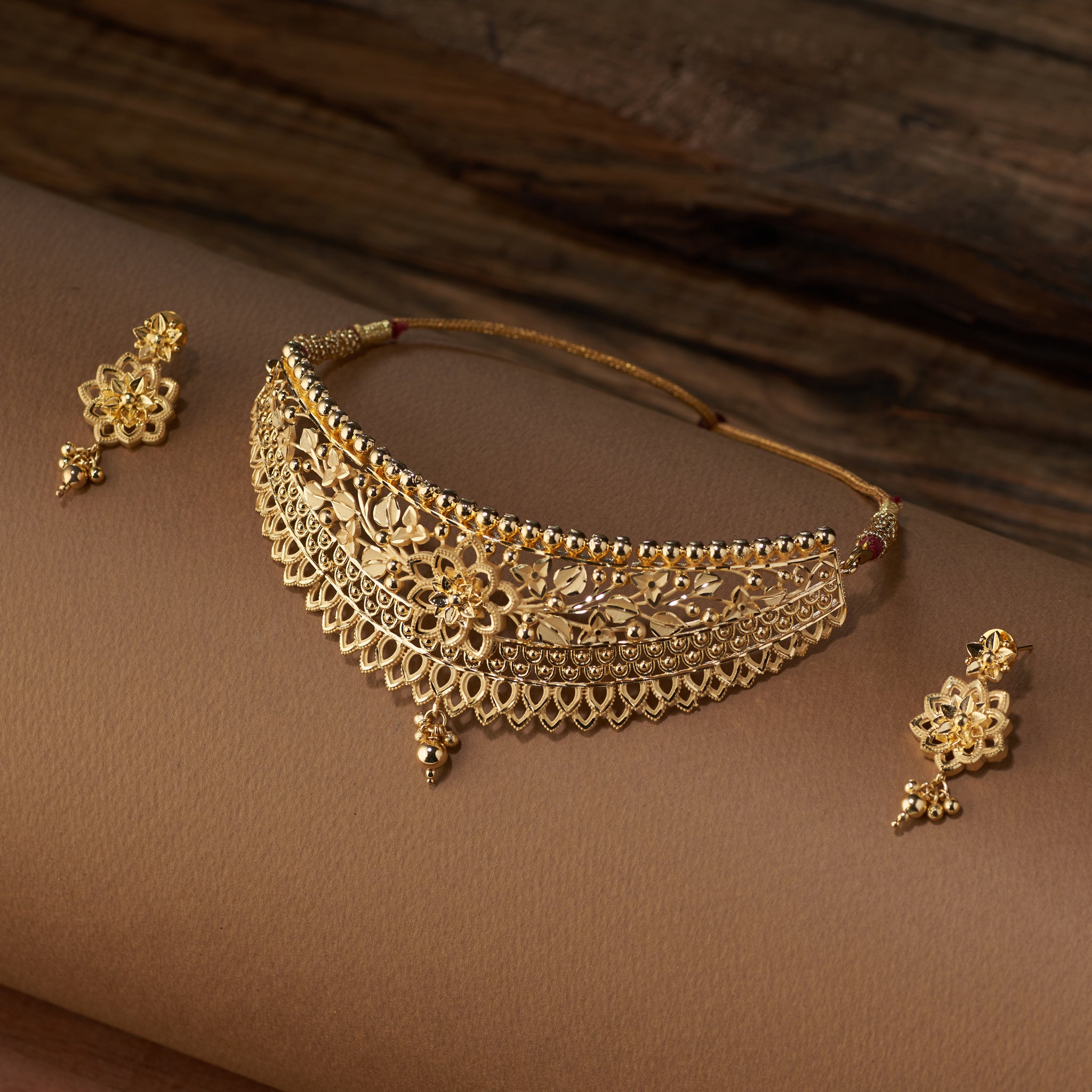 Gold choker jewellery set with necklace, earrings on a brown surface. Gold Choker, forming jewellery, Poovi by Tilloma