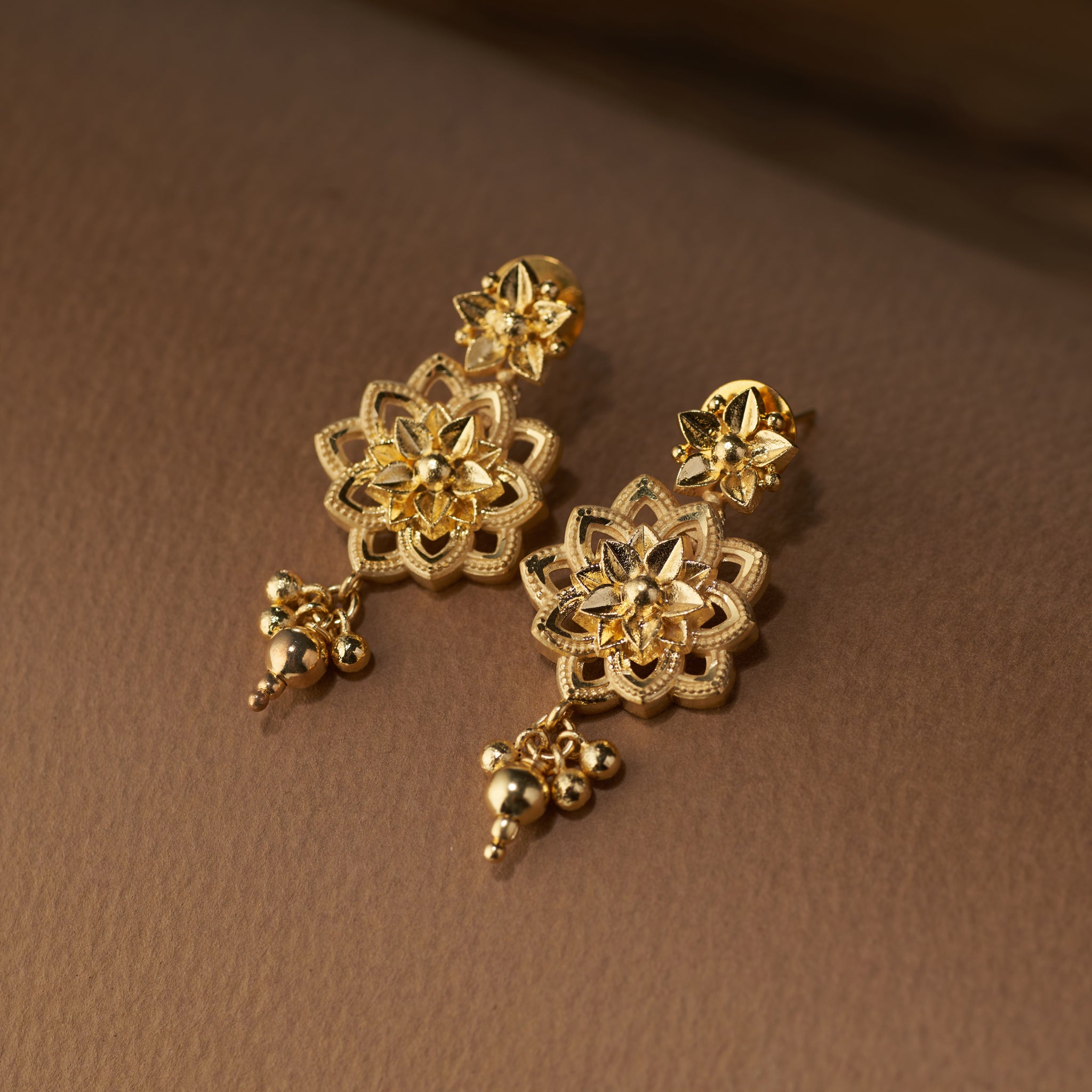 Gold floral earrings on a brown background. Gold choker jewellery set with necklace, earrings on a brown surface. Gold Choker, forming jewellery, Poovi by Tilloma.