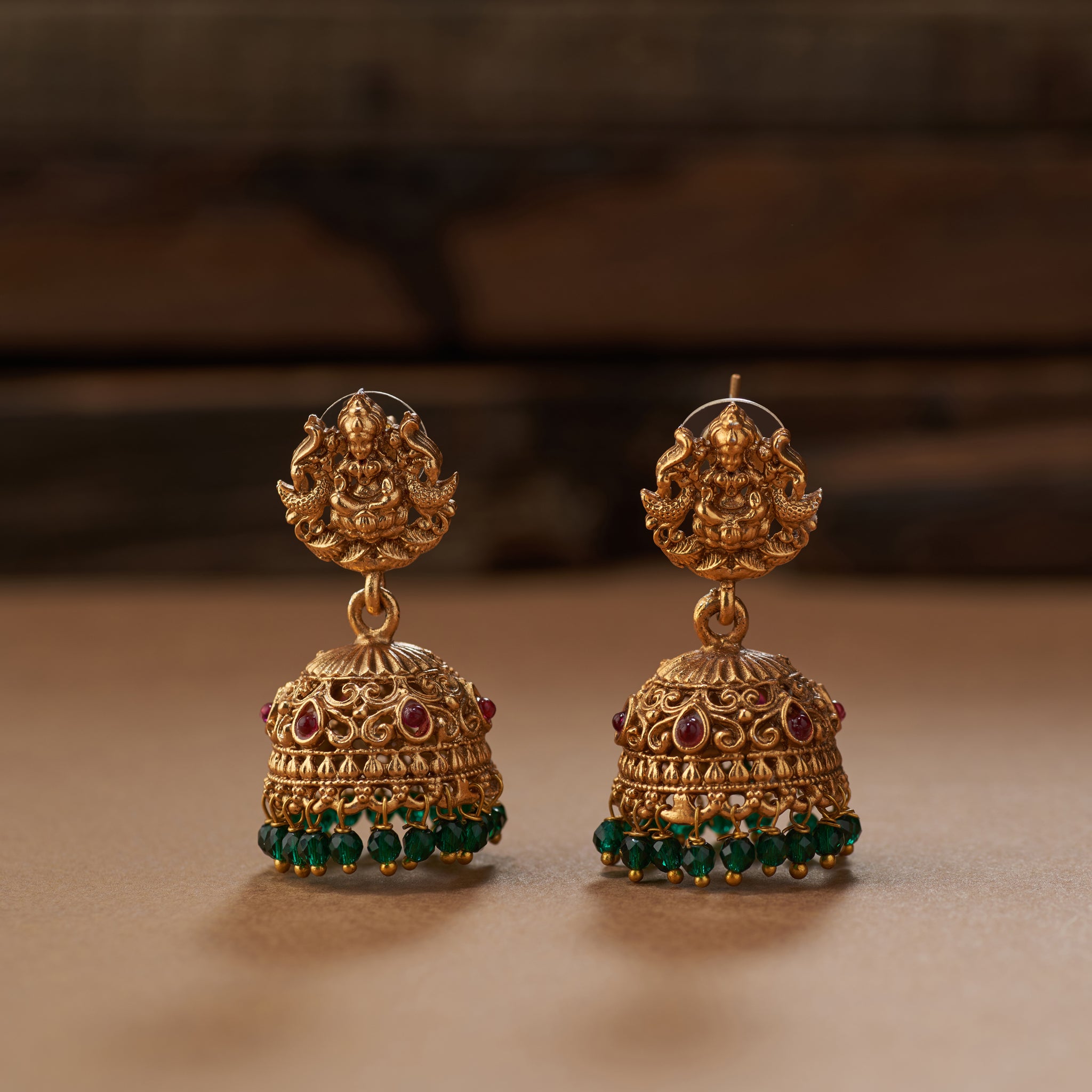 Gold earrings with green and red stones on a brown background. Gold and green beaded South Indian Temple Lakshmi necklace with matching earrings, Matt gold plated.