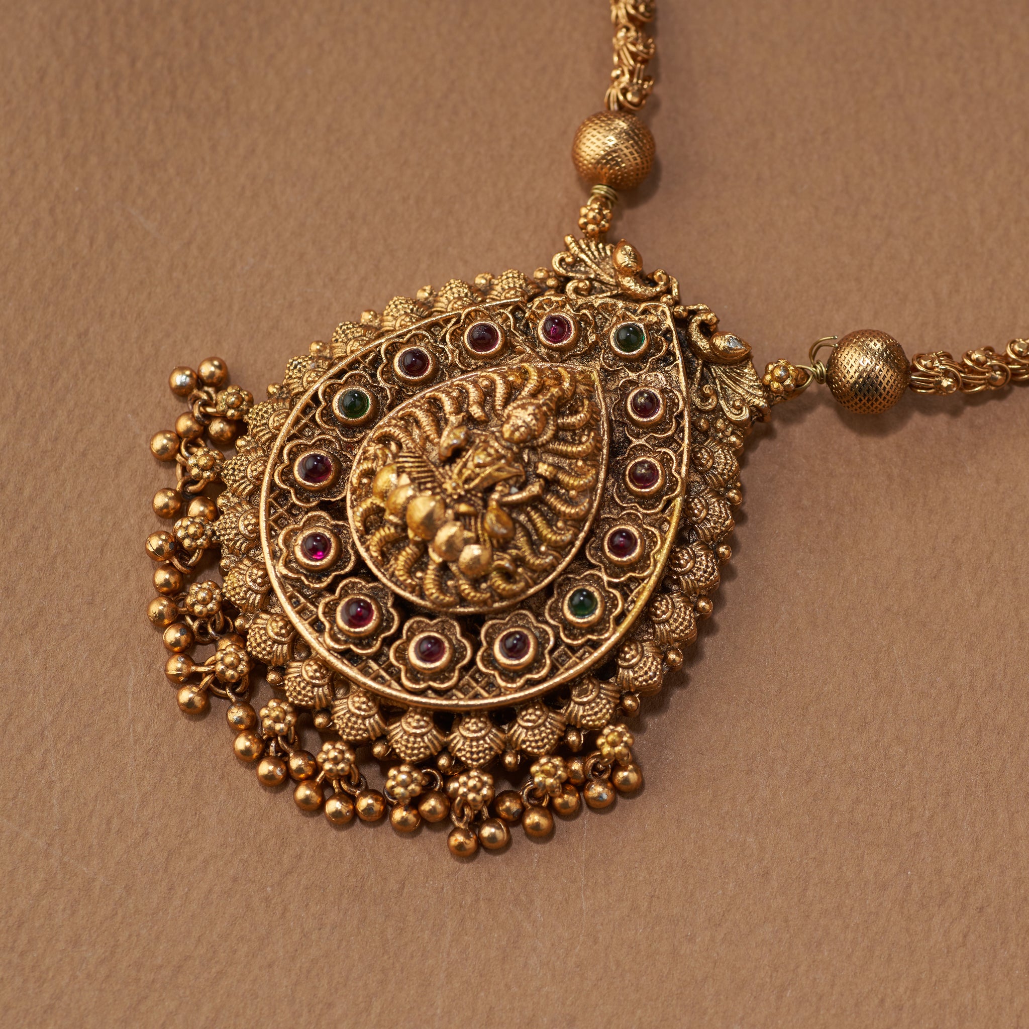 Gold necklace and earrings on a brown background. South Indian Temple jewelry with Lakshmi Motif. Temple Jewellery Lakshmi | Tilloma. Matt gold with intricate design on a brown background