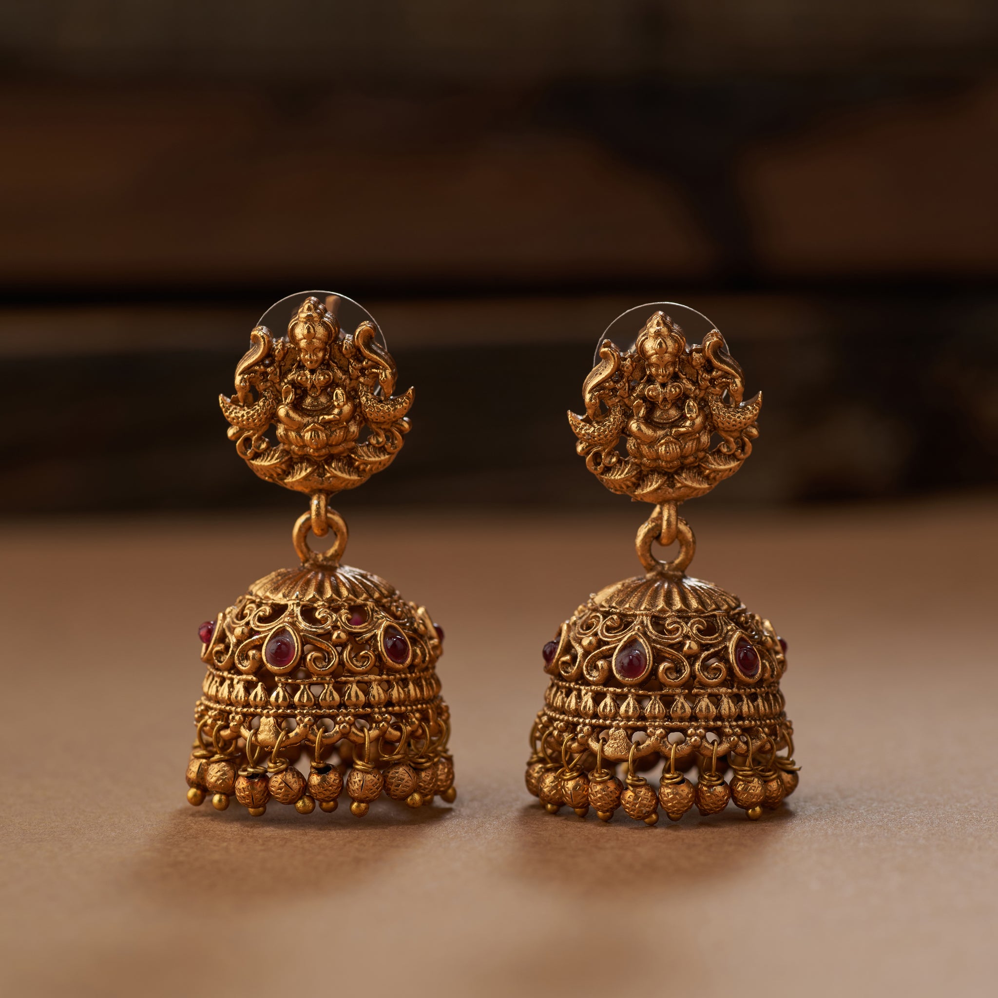 Pair of gold earrings with intricate designs on a brown background. Gold necklace and earrings on a brown background. South Indian Temple jewelry with Lakshmi Motif. Temple Jewellery Lakshmi | Tilloma. Matt gold with intricate design on a brown background
