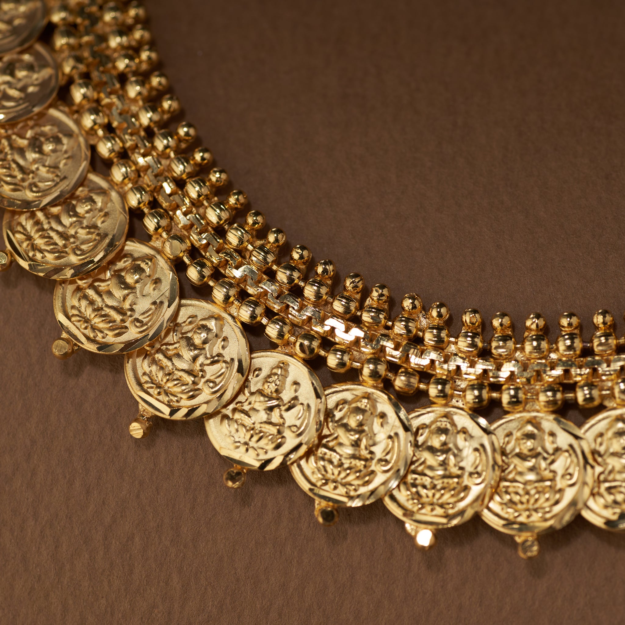 A traditional gold coin necklace set featuring a double row of detailed Lakshmi coins and a beaded chain, displayed with matching stud earrings.